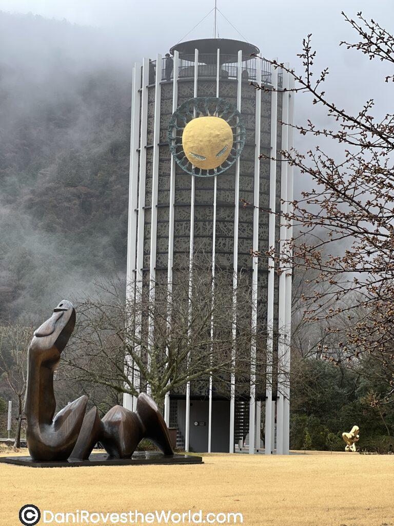 A cylindrical tower with a spiral staircase and a dramatic sculpture of a winged figure embracing a person, part of the Hakone Open-Air Museum, a must-visit day trip from Tokyo for art lovers.