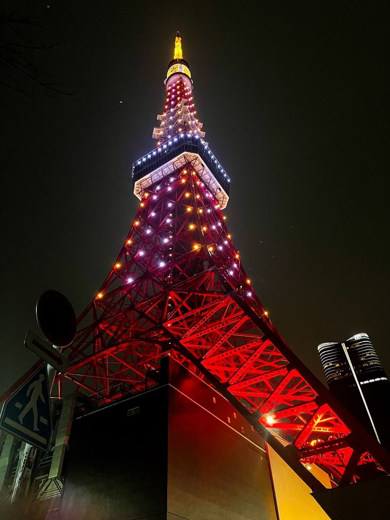 Looking up at Tokyo Tower glowing red at night in central Tokyo.