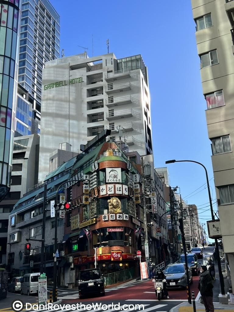 A street in Shinjuku with the Granbell Hotel rising behind colorful restaurants and neon signs, showing a lively option for where to stay in Tokyo.