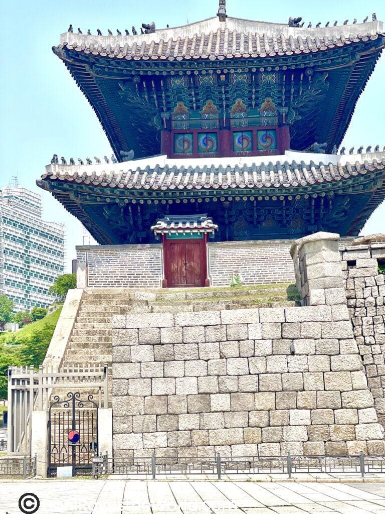 Gate to the city with traditional Korean design and stone walls, standing tall against a backdrop of modern skyscrapers. Tips for visiting Seoul: Seoul's historic gates like Sungnyemun offer a striking contrast between ancient and modern architecture.