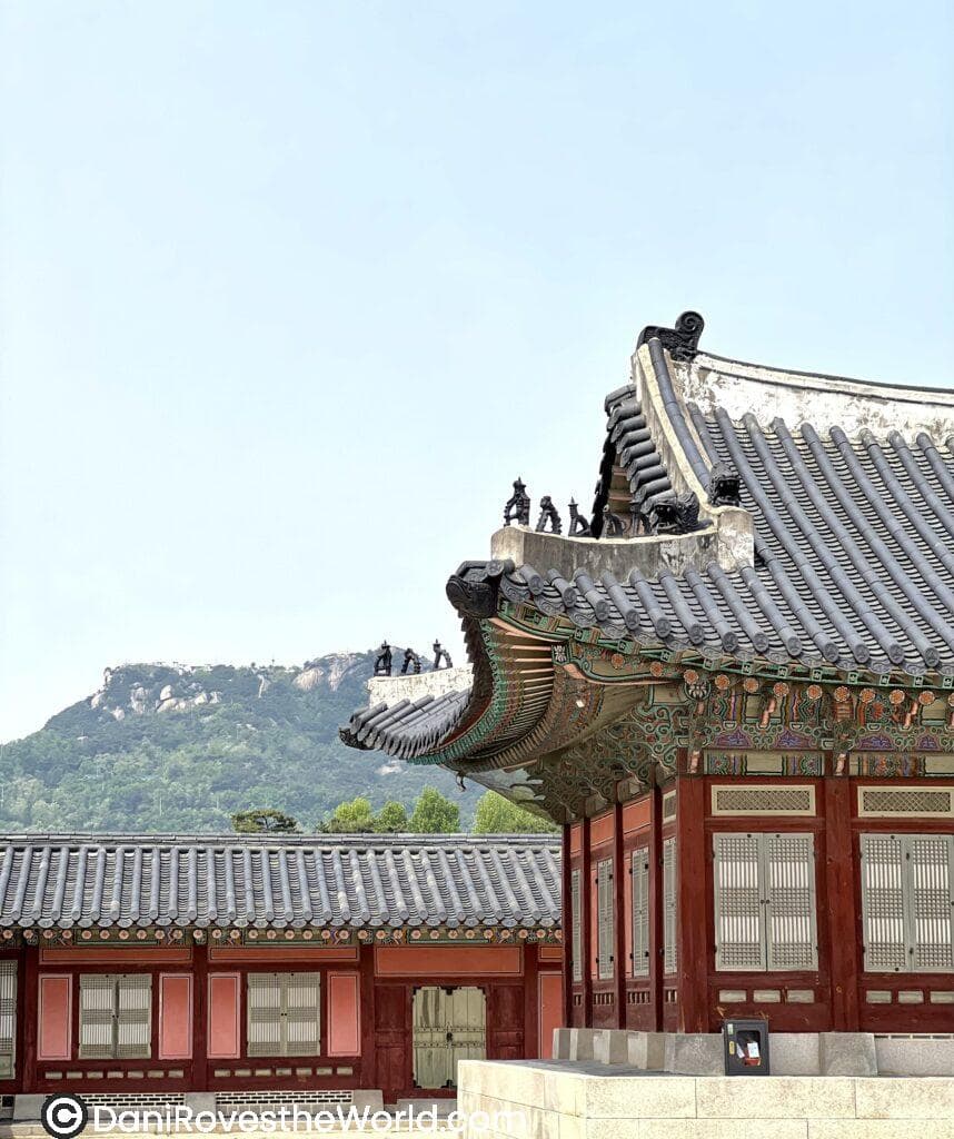 Traditional Korean palace architecture at Gyeongbokgung Palace Palace in Seoul, showcasing intricate wooden beams and vibrant painted details check out the figurines on top of the building and the mountains behind the palace. A must-visit cultural experience when exploring Seoul.