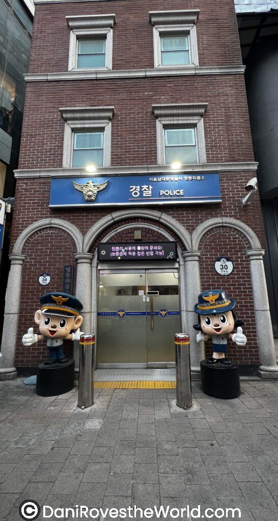 a cartoon like statue stands in front of the myeongdong walking street police station. this friendly sculpture is welcoming
