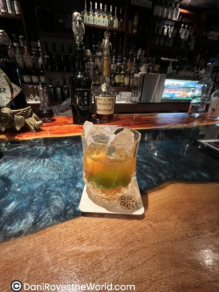 A vibrant speakeasy craft cocktail bar. The drink is an old fashion with a citrus garnish served over ice in a textured glass at a Kyoto cocktail bar.