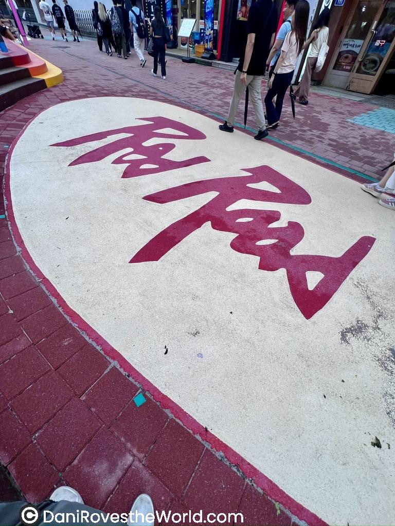 Sidewalk in Hongdae, Seoul, featuring 'The Road' written in bold red lettering, symbolizing the area's vibrant street culture and a popular destination for solo female travelers to explore.