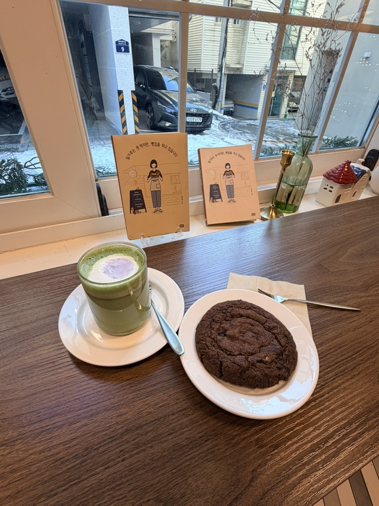 Matcha latte and chocolate cookie at a cozy café in Seoul with a window seat overlooking a quiet winter street.