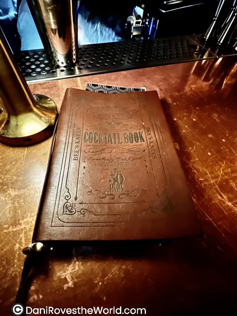 A leather-bound cocktail book labeled 'Bee's Knees Cocktail Book' resting on a polished bar top in a Kyoto cocktail bar. The vintage design and elegant ambiance highlight the sophisticated cocktail experience offered at this bar.