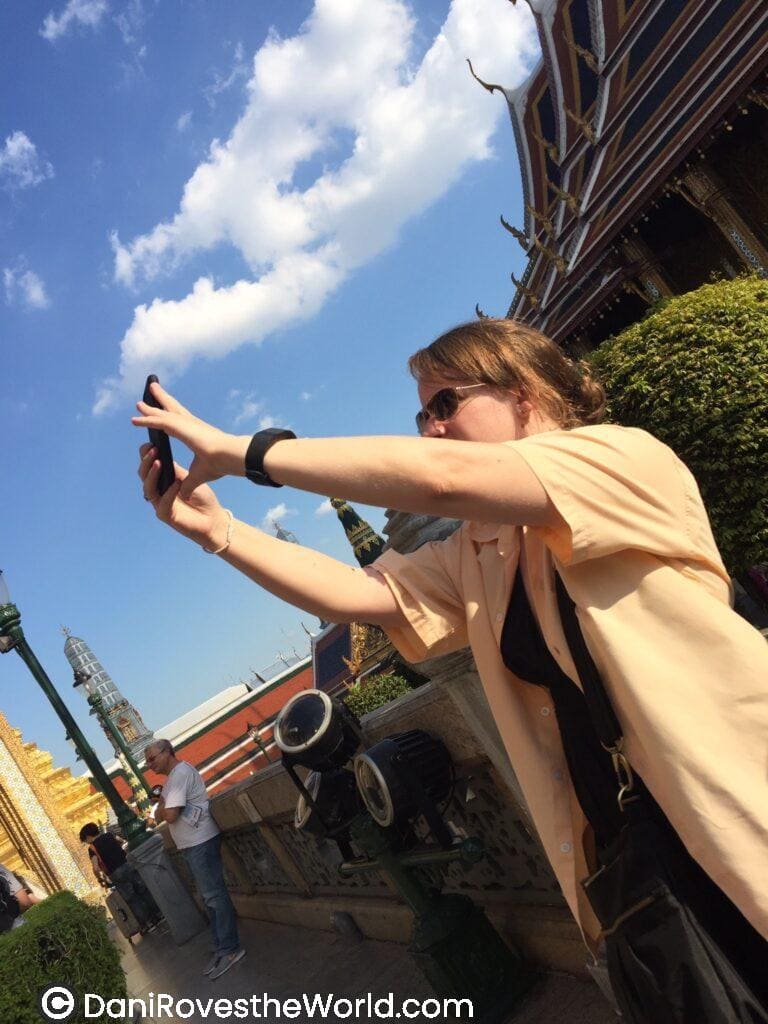 Dani in front of the Banglok Palace under a clear blue sky. Wearing sunglasses and casual attire, she captures her adventure at a famous cultural site. Taking photography is a great budget hack for solo female travelers to document their journeys without spending extra money.