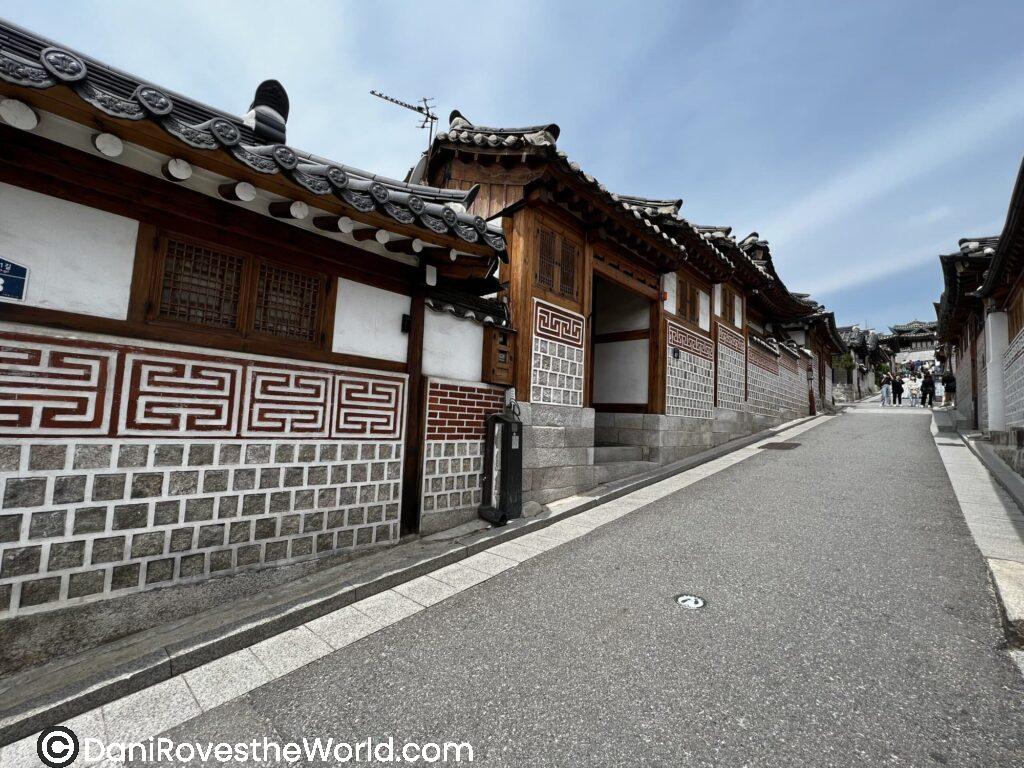 A serene alley in Bukchon Hanok Village lined with traditional Korean hanok houses, their curved tiled roofs and wooden frames exuding historical charm.