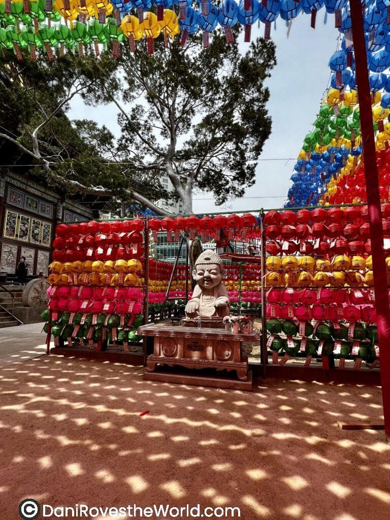  A small Buddha statue displayed beneath a colorful canopy of lanterns in Seoul during a festival celebration. This image captures the essence of Seoul’s vibrant spring festivals, such as the Lotus Lantern Festival, a perfect time for visitors to experience local traditions.