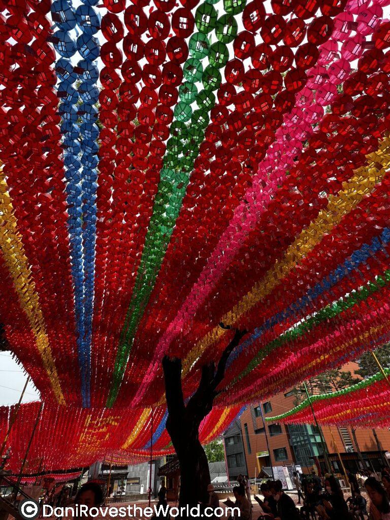Overhead view of red, green, blue, and pink lanterns cascading in rows, creating a colorful canopy in a temple courtyard during a festival. This vibrant display is typical of Seoul’s spring festivals, like the Lotus Lantern Festival, making it an ideal time for visitors.