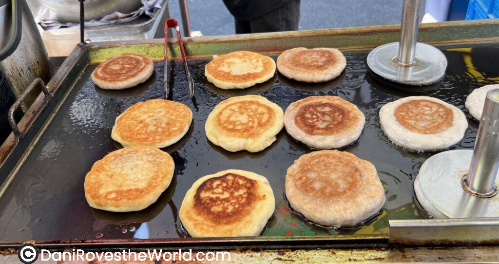 My favorite street food, Hotteok, Korean sweet pancakes filled with sugar, cinnamon, and nuts, frying on a griddle, a must-try street food in Seoul's bustling markets.