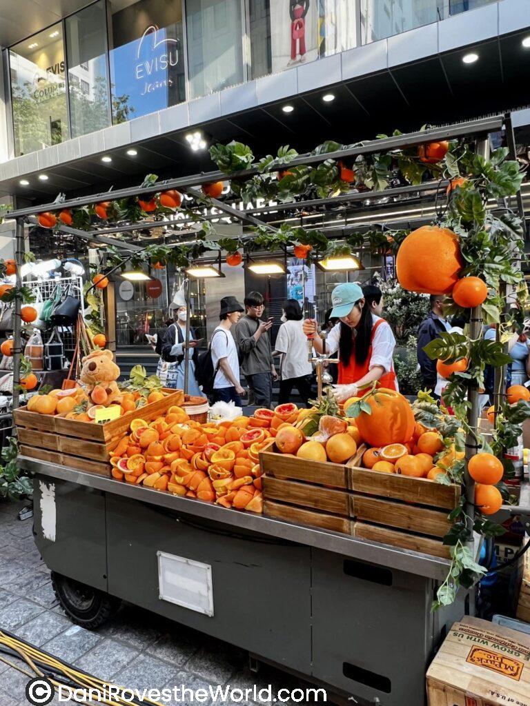 food stall selling fresh orange juice in Myeongdong, Seoul, a refreshing treat to enjoy on your one-day food tour of the city.