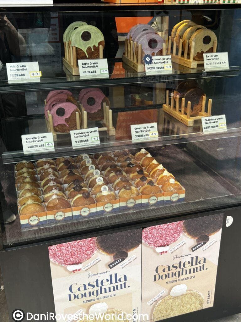 Colorful New York rolls and Castella doughnuts on display at a bakery in Hongdae, Seoul, offering unique dessert flavors like apple cream and sweet potato for solo female travelers to enjoy
