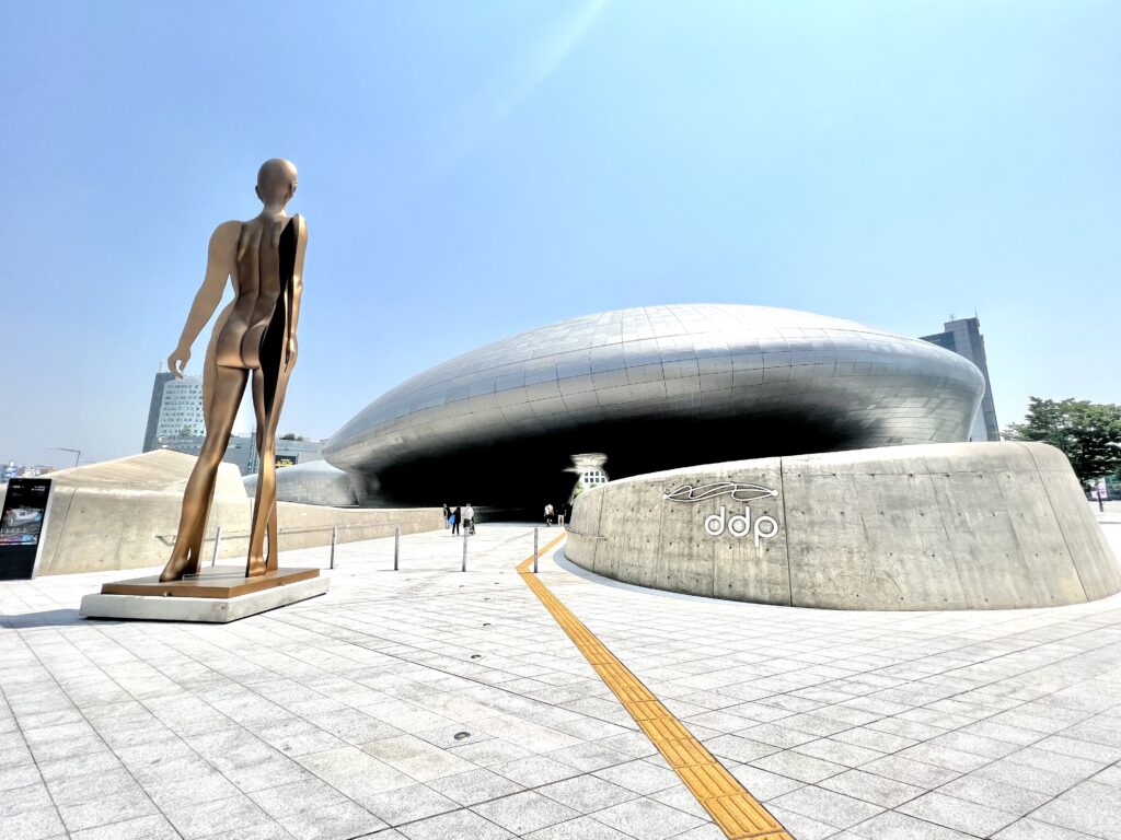 Dongdaemun Design Plaza (DDP) in Seoul, a futuristic architectural wonder, accompanied by a modern bronze statue—an unmissable experience in Seoul.