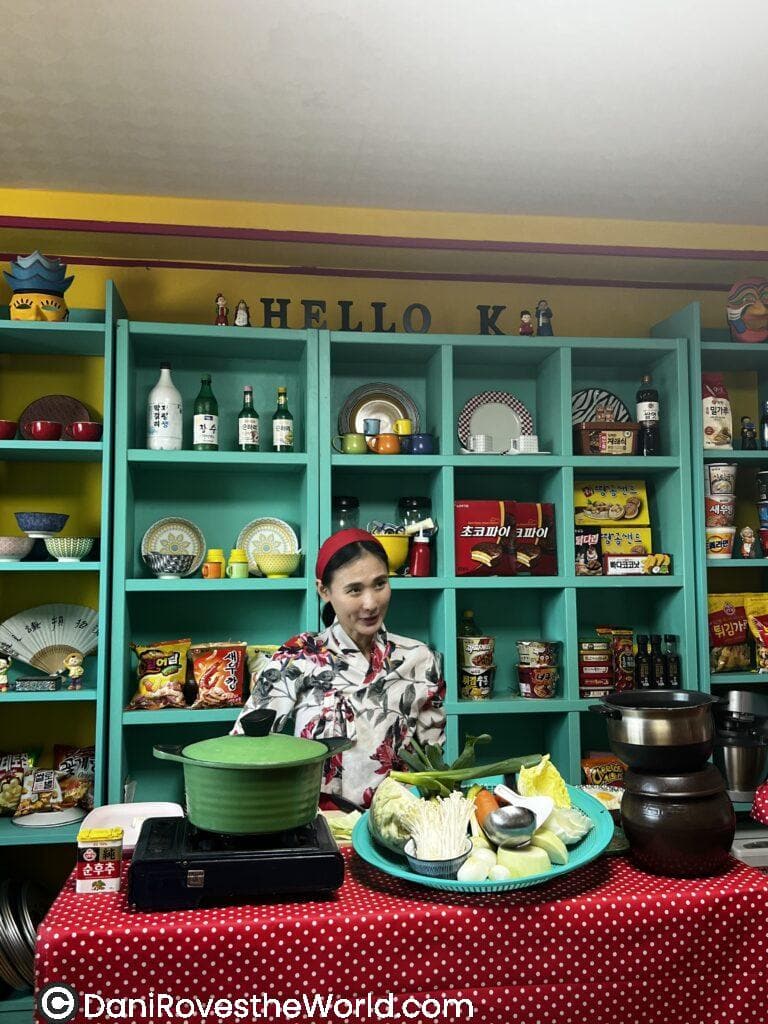 Korean cooking instructor surrounded by ingredients and cookware, preparing to teach traditional dishes in a lively Korean cooking class