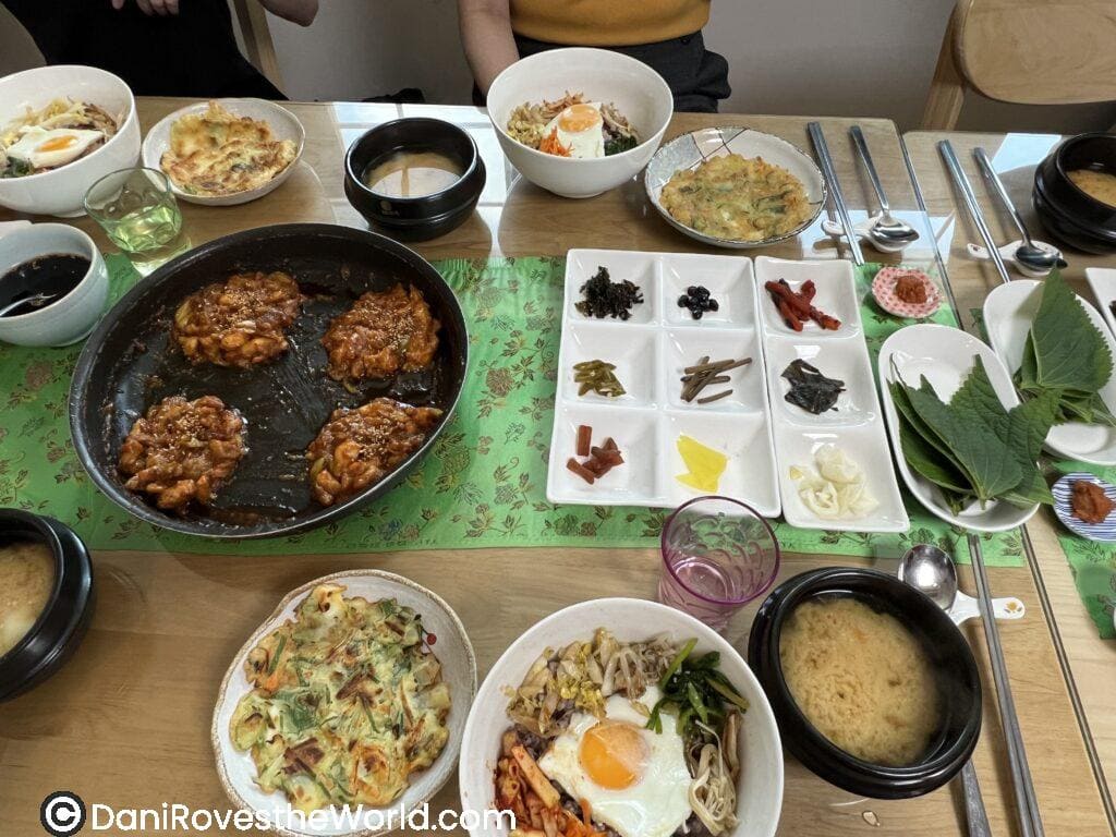 A table full of freshly prepared Korean dishes, including bibimbap and pancakes, made during a Korean cooking class
