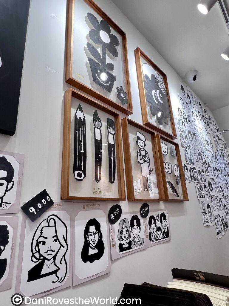 Acorn Caricature, Myeongdong, Seoul
A gallery wall of caricatures inside Acorn Caricature located in Myeongdong shop featuring framed black-and-white caricatures and art pieces, showcasing creative local artwork. Visiting this art store is one of the unique things to do in Myeongdong, ideal for art lovers seeking personalized souvenirs