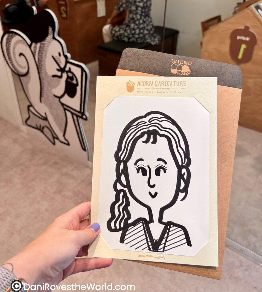 A hand holding a black-and-white caricature portrait from Acorn Caricature in Myeongdong. This popular caricature shop offers customized artwork, a fun activity and keepsake for visitors exploring things to do in Myeongdong