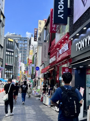 A bustling outdoor shopping street in Myeongdong, filled with shops like TONYMOLY and Pretty Skin, alongside towering signboards and people walking past. Myeongdong is famous for its beauty products, making shopping one of the top things to do in Myeongdong