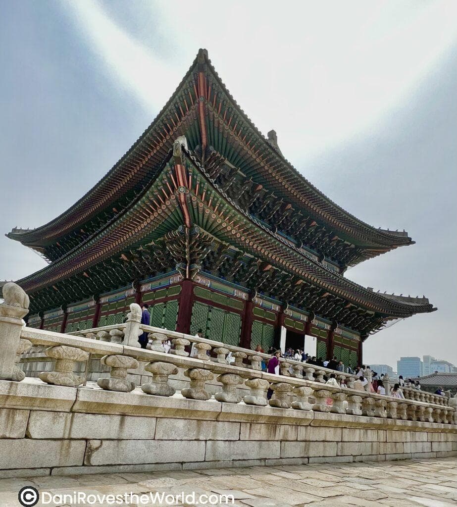 A wide-angle view of Gyeongbokgung Palace in Seoul, with its ornate roof and large courtyard, surrounded by visitors. An essential stop when planning your 24 hours in Seoul itinerary.