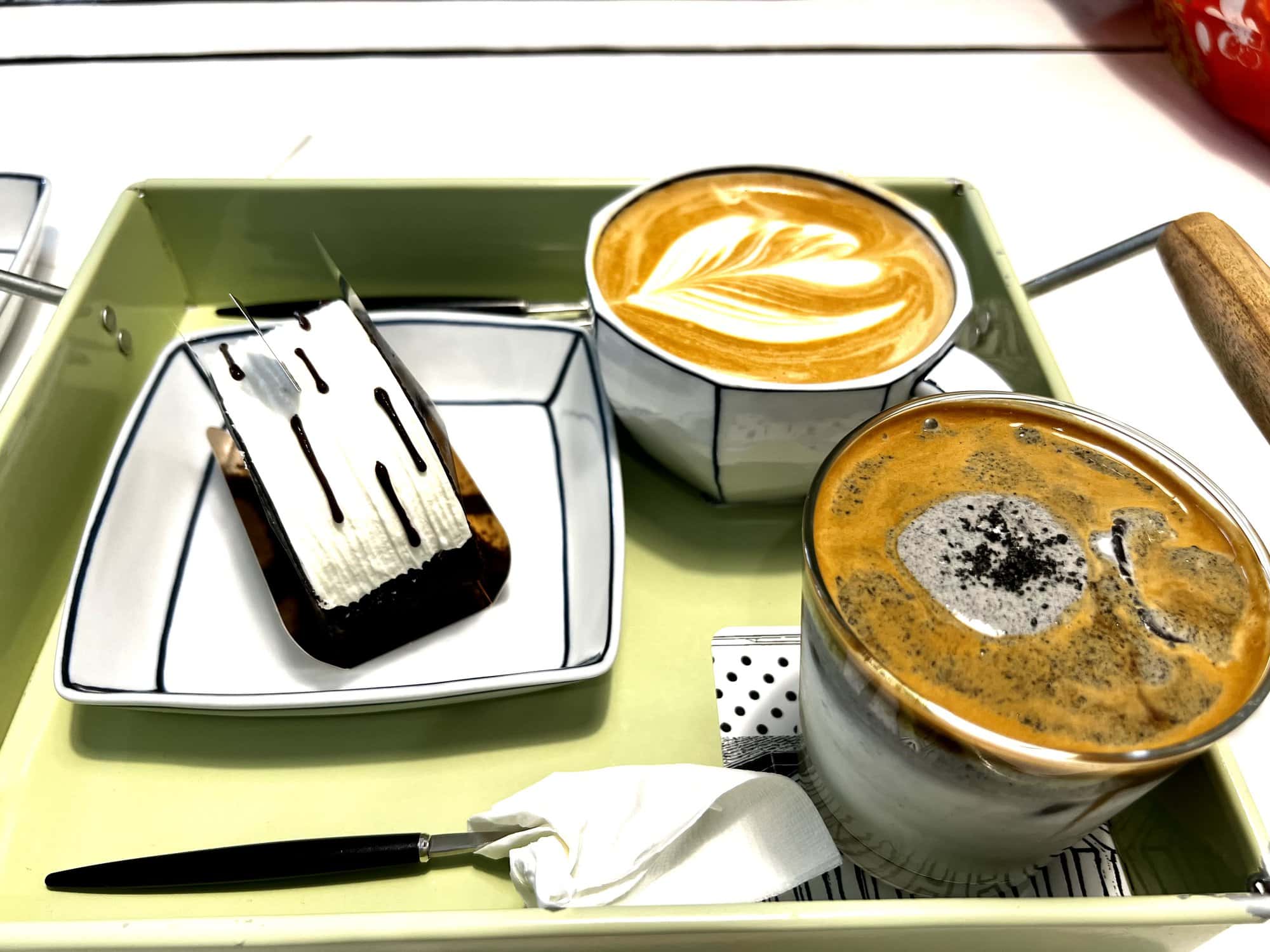 A tray with a beautifully presented cappuccino, iced coffee, and a chocolate dessert at a café in Seoul,