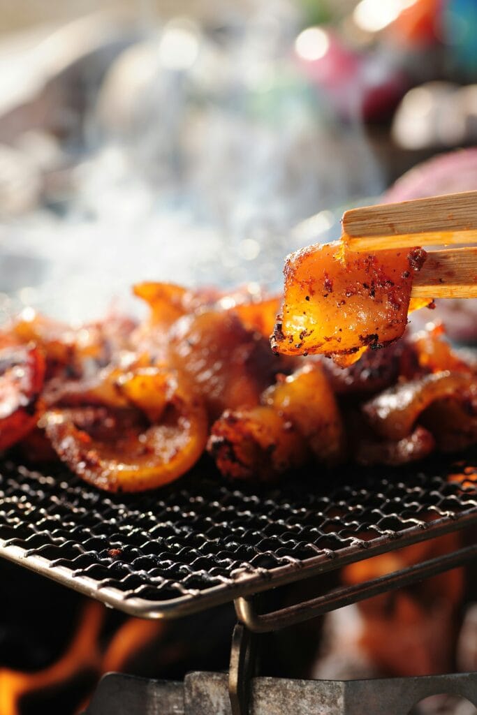 Close-up of sizzling pork belly slices grilling on a mesh wire grill at a Korean BBQ. The perfect caramelization and smoke enhance the rich flavors of the meat.