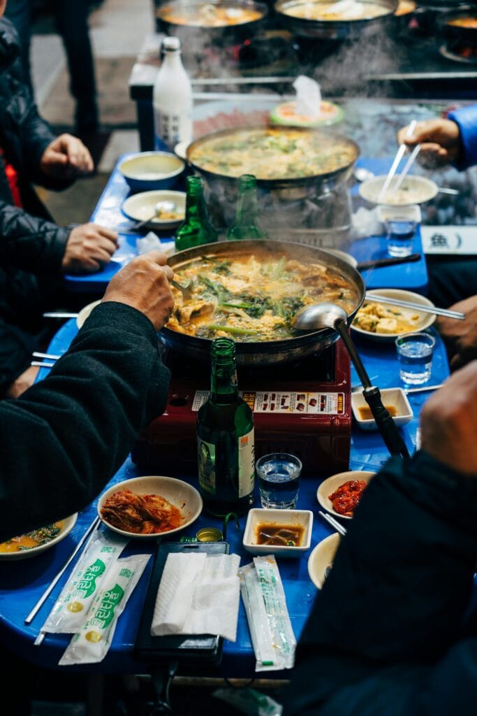A group of people gathered around a table in Seoul, enjoying a communal hotpot meal with traditional Korean side dishes. The image highlights the importance of shared dining experiences in Korean culture.