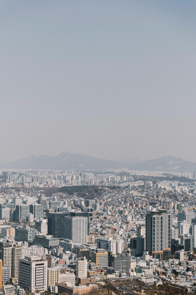 A panoramic view of Seoul from above, featuring a mix of modern skyscrapers and distant mountains. Experience the historical transformation of the city from its ancient roots to modern times during 24 hours of history in Seoul.
