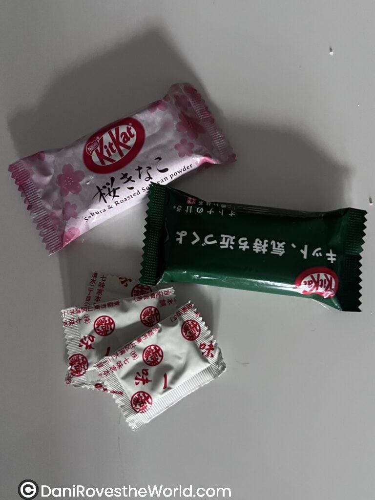 A collection of Japanese candies, including a pink KitKat bar with "Sakura & Roasted Soybean Powder" and a green one alongside individually wrapped red and white treats.