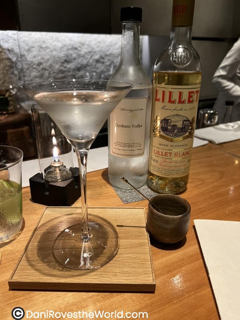 A refined Tokyo cocktails setup, featuring a martini glass filled with a clear drink, alongside Gyokuro Vodka and Lillet Blanc. The elegant arrangement on a wooden board highlights the sophistication of Tokyo bars and their creative cocktail offerings.