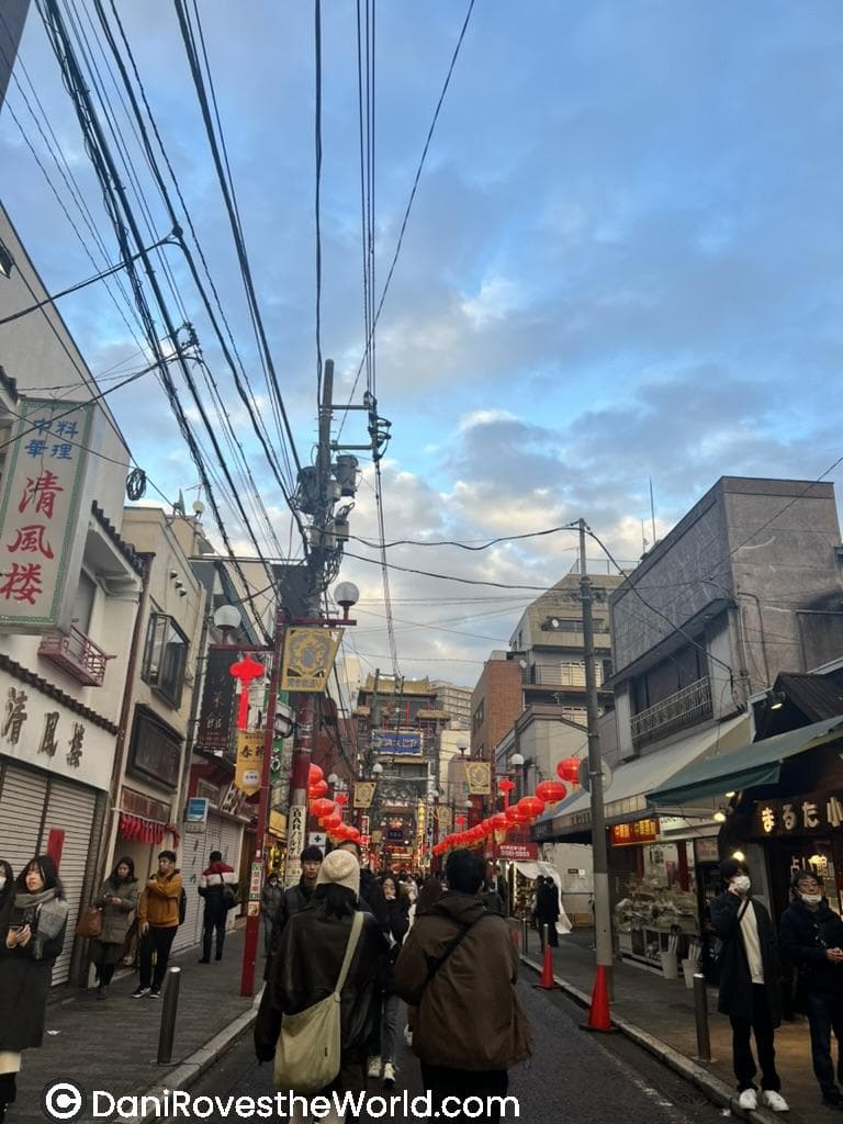  A lively shopping street in Yokohama’s Chinatown, adorned with vibrant red lanterns, colorful signs, and a bustling crowd enjoying the festive ambiance.