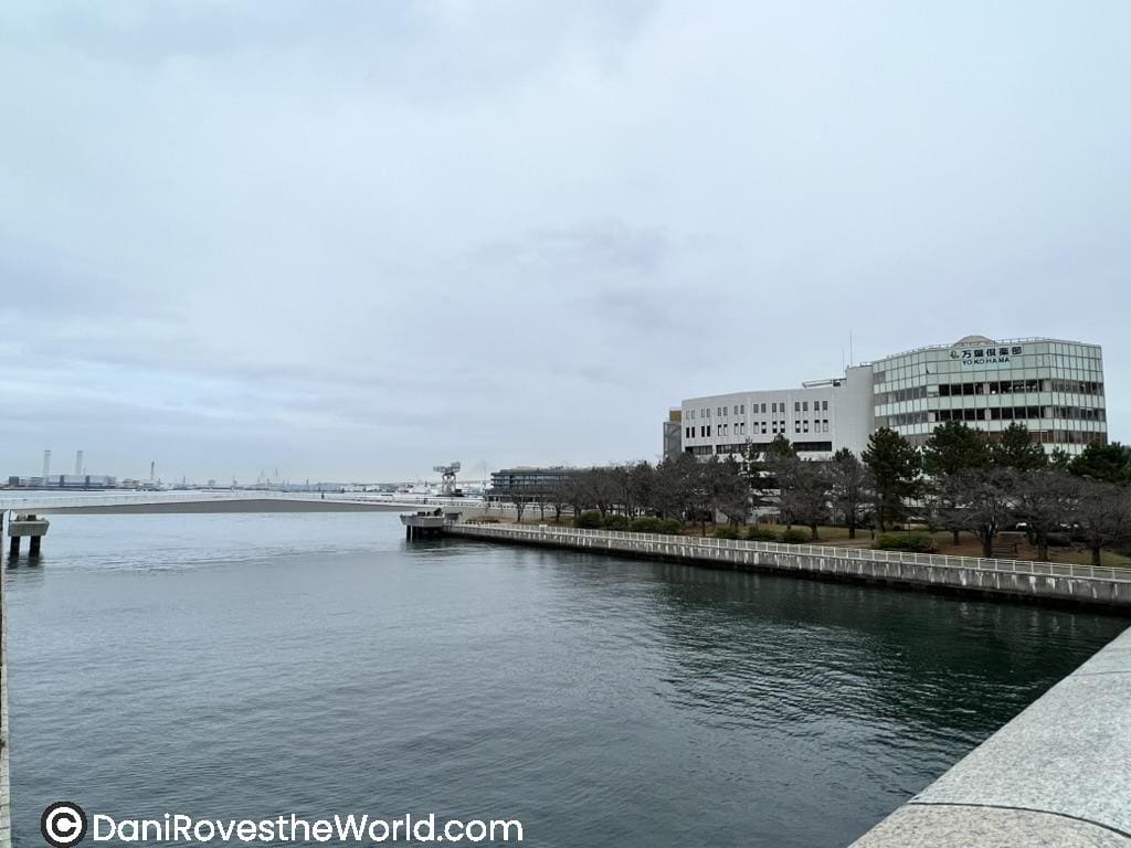 A view of Yokohama's waterfront featuring modern buildings, a calm waterway, and a cloudy sky, creating a tranquil yet urban atmosphere.