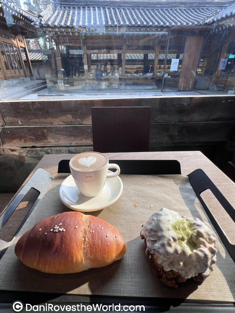 Display trays in a Seoul coffee shop are filled with colorful pastries, including croissants topped with green grapes, orange slices, and powdered sugar, showcasing a vibrant selection of fruit-topped desserts.