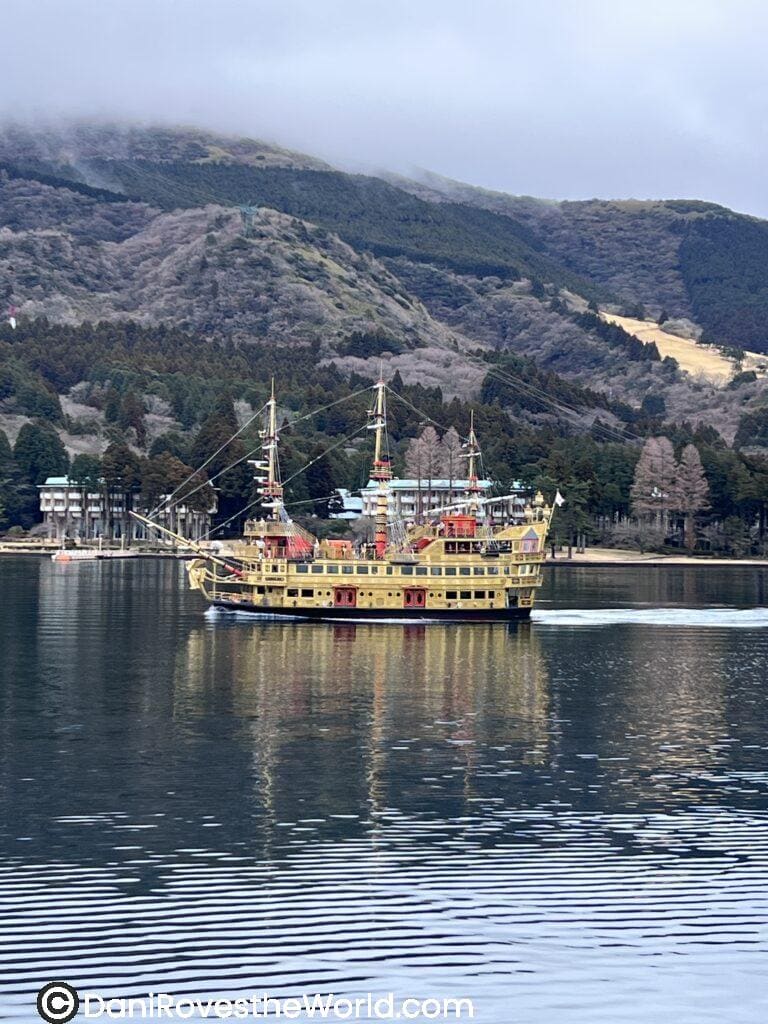 A colorful pirate-style sightseeing cruise ship gliding across the calm waters of Lake Ashi, with misty mountains in the background—an iconic part of a day trip to Hakone from Tokyo.
