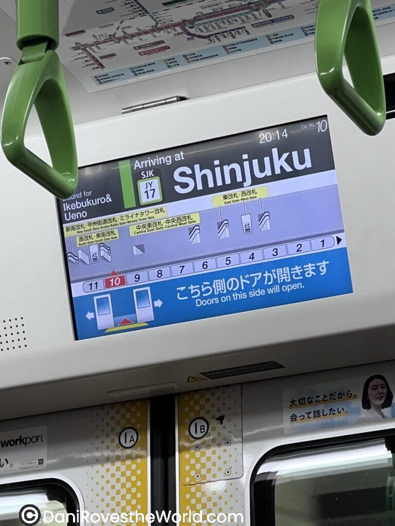 A digital screen inside a JR train shows arrival information for Shinjuku Station, listing connecting lines including the Chuo Line, Marunouchi Line, and Toei Oedo Line. The screen displays gate directions, platform numbers, and train car information, helping passengers efficiently navigate Tokyo’s complex transit system.