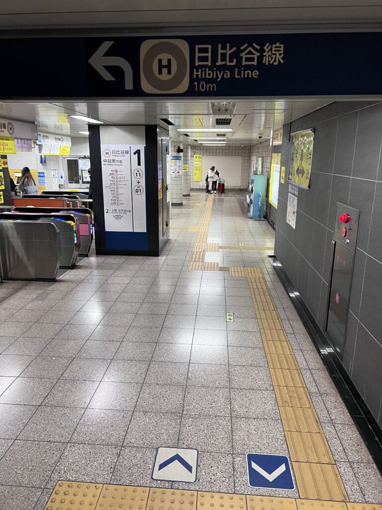 A Tokyo subway entrance sign shows the logos of both Toei Subway and Tokyo Metro above directional arrows leading to various lines, indicating shared station access. This signage helps riders identify the correct entrances for different subway networks in Tokyo.