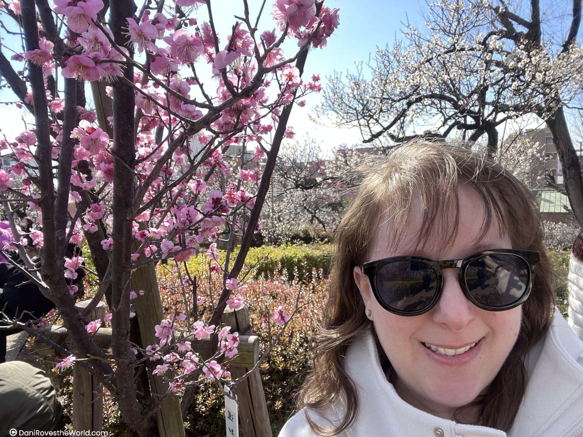 Dani taking a selfie in front of blooming pink plum blossoms in Tokyo, capturing seasonal beauty while exploring neighborhoods for where to stay in Tokyo.