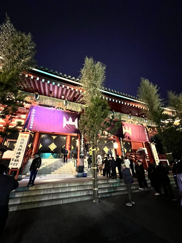 Night view of Senso-ji Temple’s main hall beautifully lit with purple drapes and glowing lanterns, as visitors climb the steps. A magical moment captured while exploring Asakusa after dark.