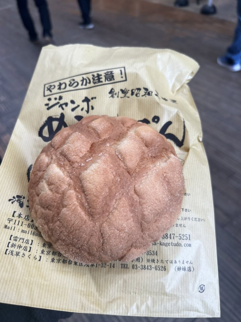Close-up of a golden, sugar-dusted jumbo melon pan resting on branded bakery paper from Kagetsudo in Asakusa. A must-try sweet snack when exploring Asakusa’s famous street food scene.