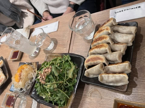 Grilled gyoza dumplings lined up on a plate next to a fresh mizuna salad and pickled sides, part of a shared meal on a Tokyo izakaya tour.