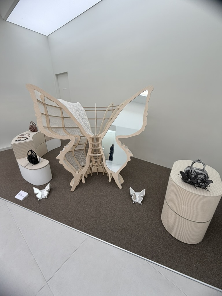 Butterfly inspired art installation featuring a wooden sculptural frame with mirrored wings displayed in a minimalist gallery space.