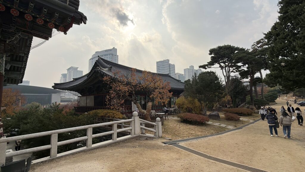 Historic temple structure at Bongeunsa Temple surrounded by trees with tall Seoul skyscrapers rising behind it.