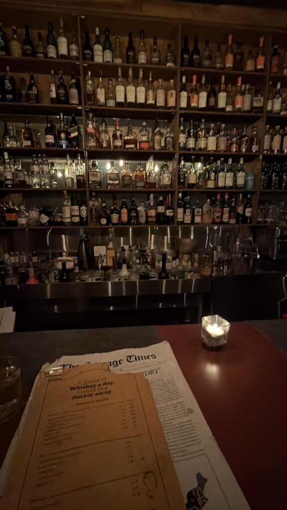 Moody whiskey bar in Seoul with floor to ceiling shelves of bottles and a candlelit bar counter atmosphere.